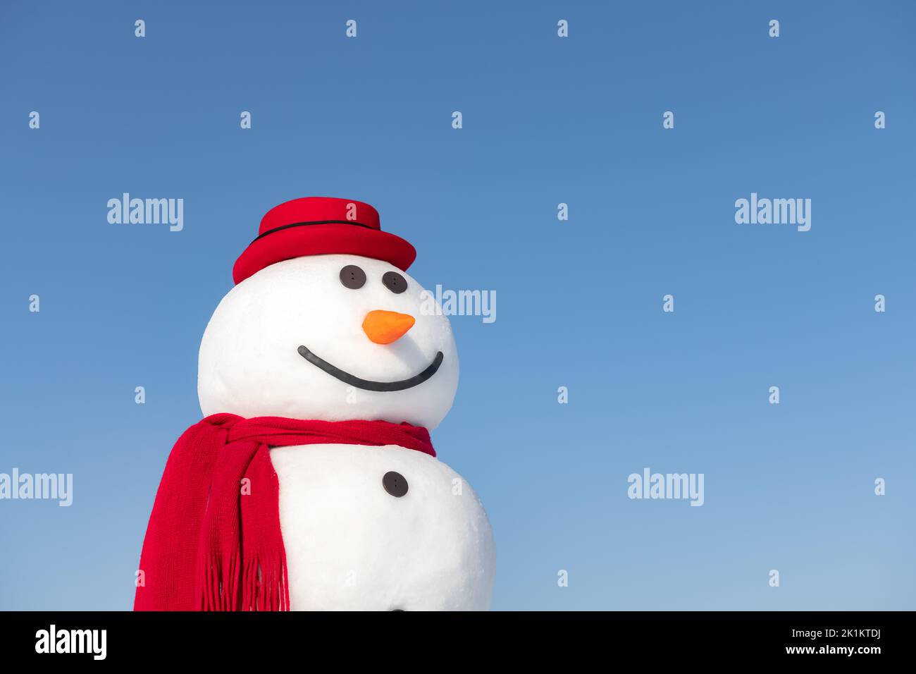 Muñeco de nieve divertido con un sombrero rojo con estilo y un tapón con escalfón rojo sobre fondo azul cielo Foto de stock