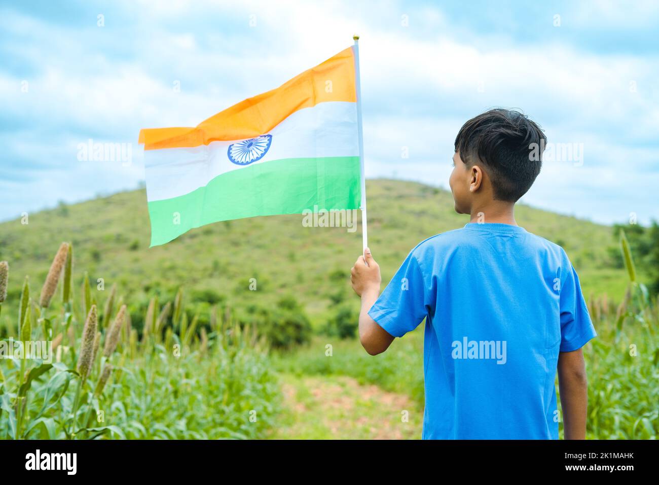 Foto trasera de un niño con bandera india en una granja cerca de la montaña verde - concepto de día de la república, libertad y patriotismo Foto de stock