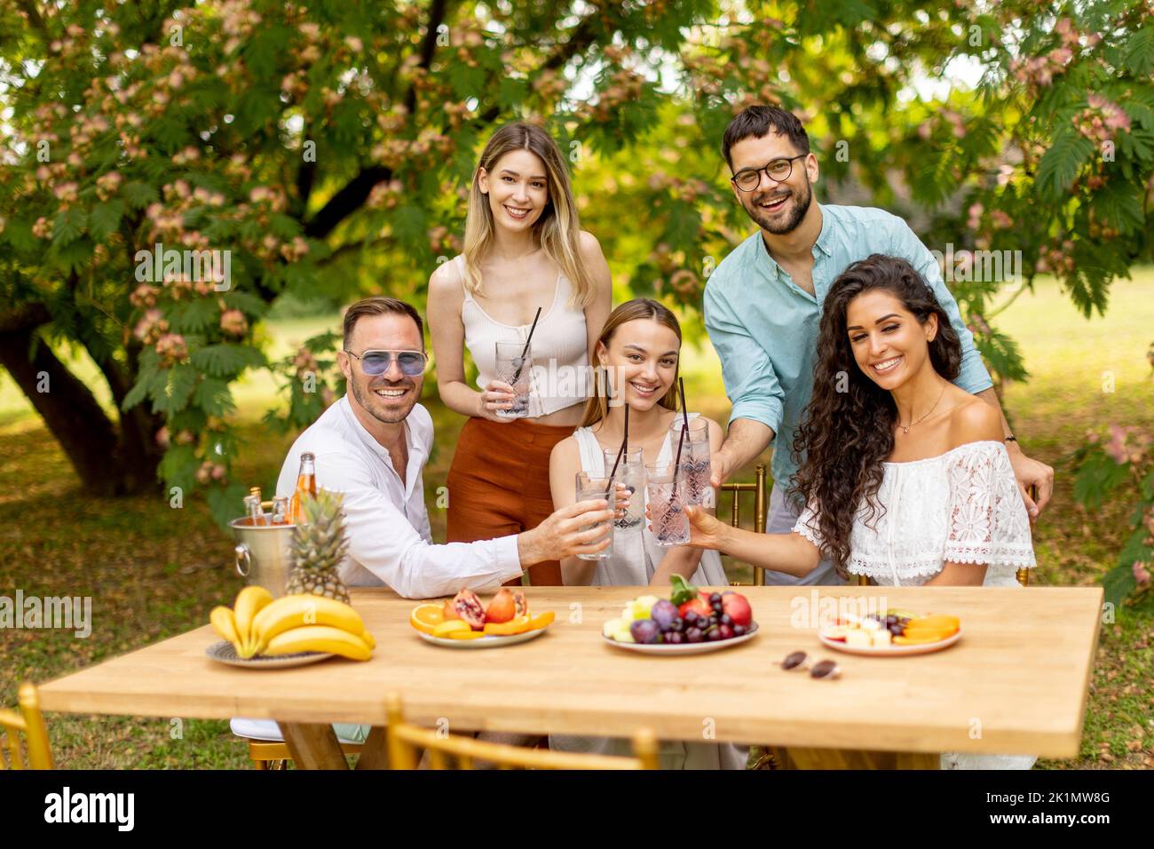 Grupo de jóvenes alegrando con limonada fresca y comiendo frutas en el jardín Foto de stock