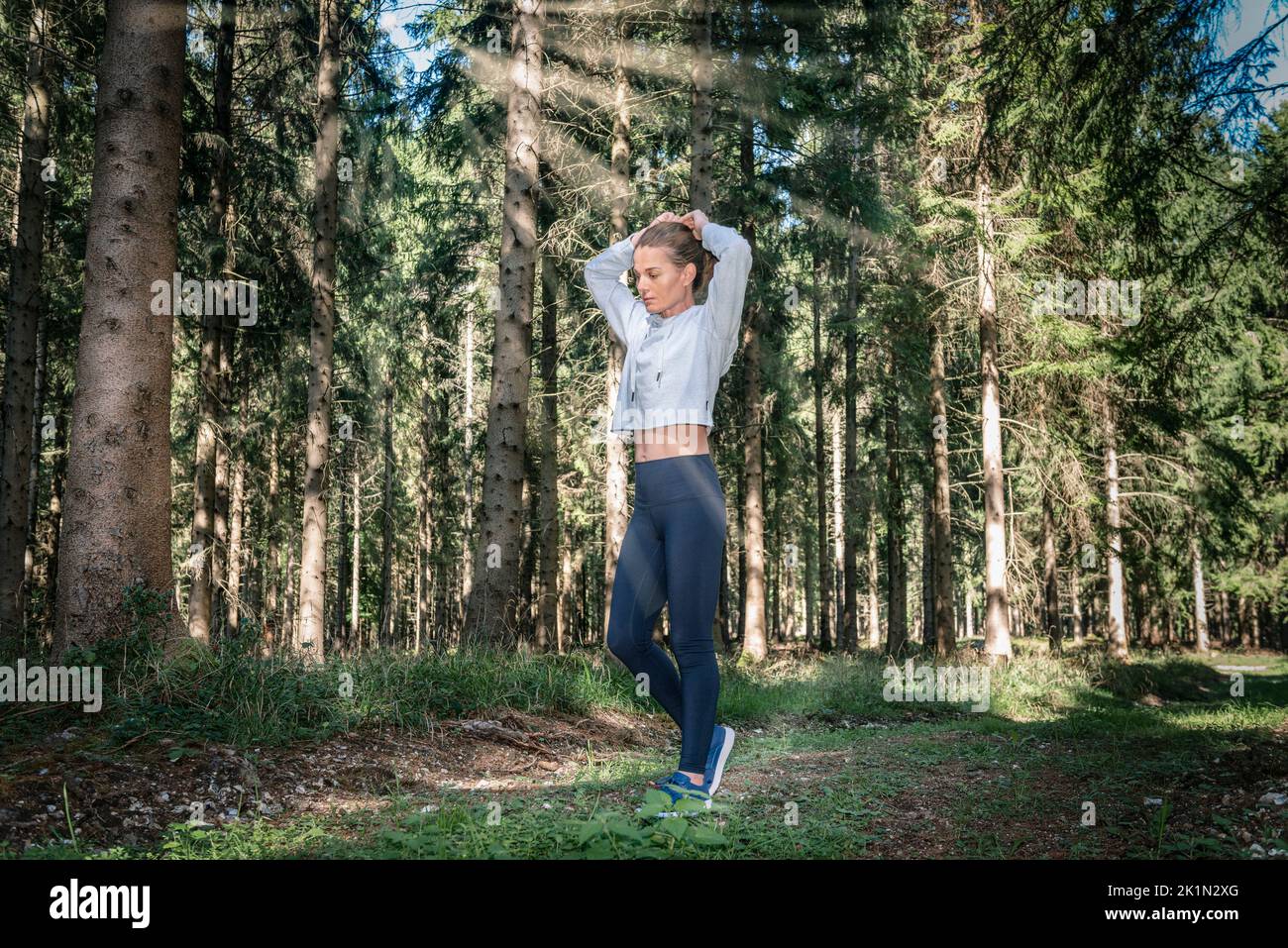 Mujer deportiva atando su cabello antes de hacer ejercicio en un bosque. Foto de stock