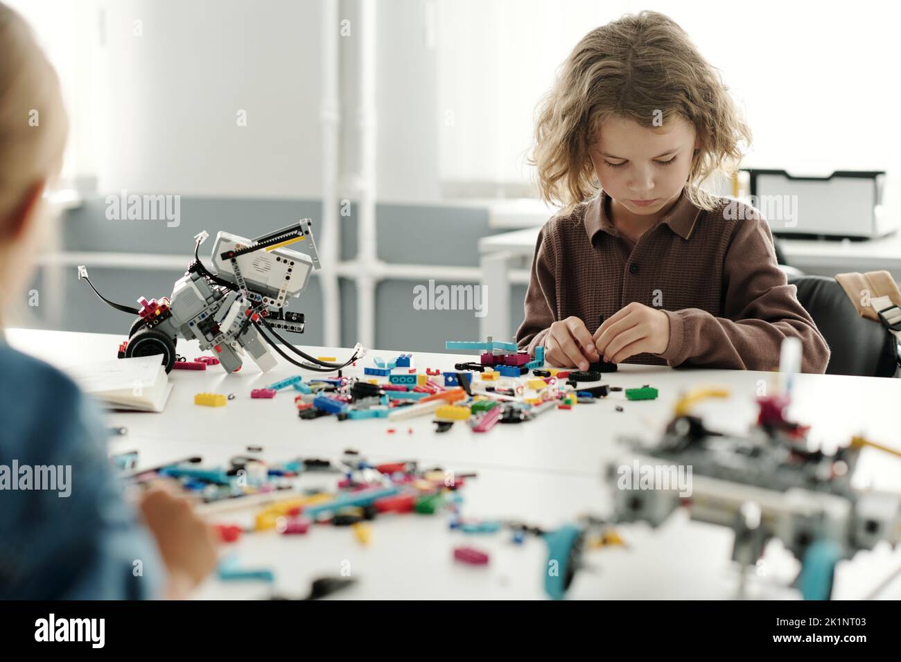 Inteligente colegio sentado junto al escritorio y conectando los detalles del robot mientras construye un nuevo juguete electrónico en la lección de robótica Foto de stock