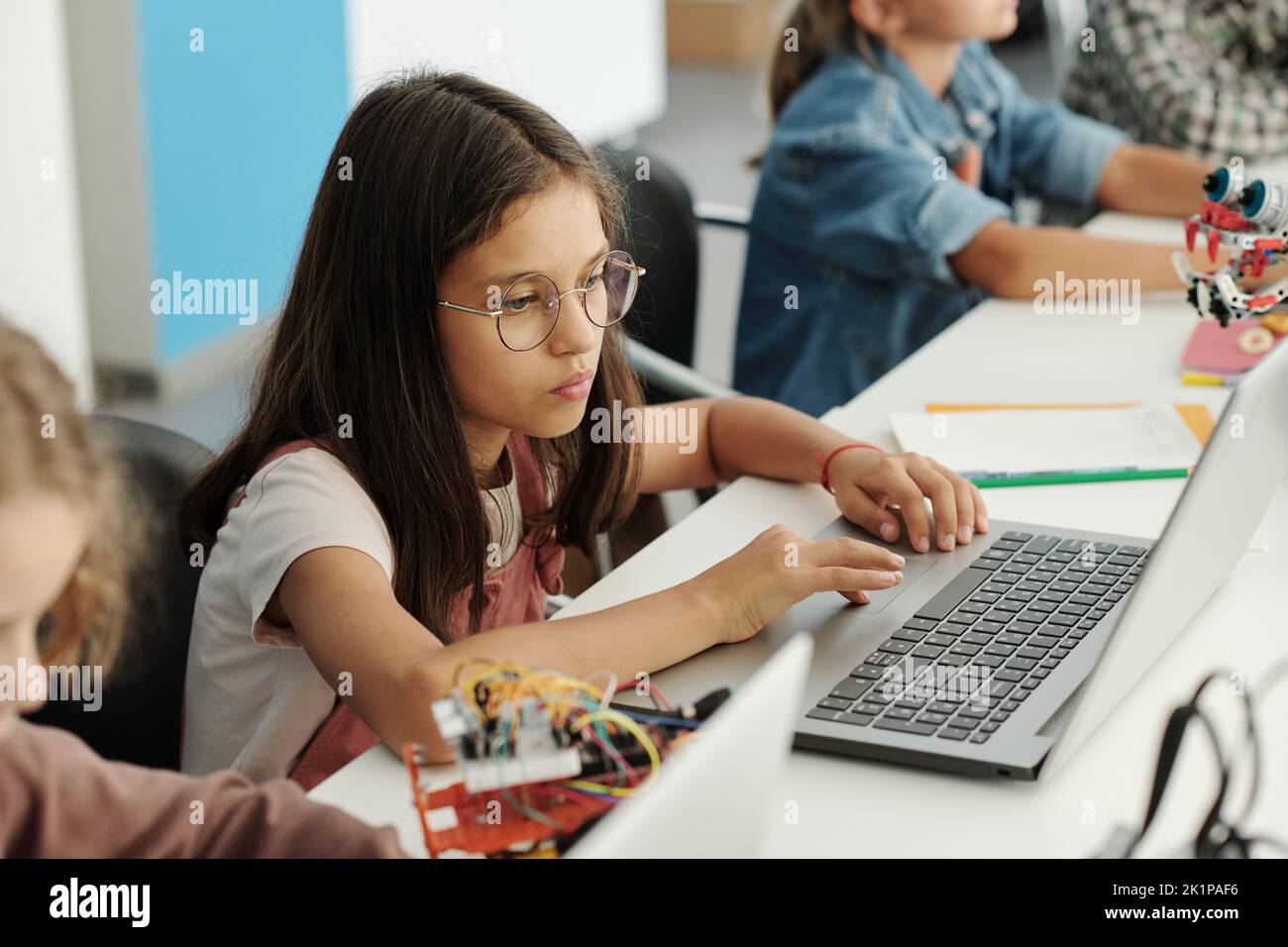Estudiante inteligente serio en gafas mirando la pantalla del ordenador portátil durante la red o la preparación de la presentación del proyecto en la lección Foto de stock