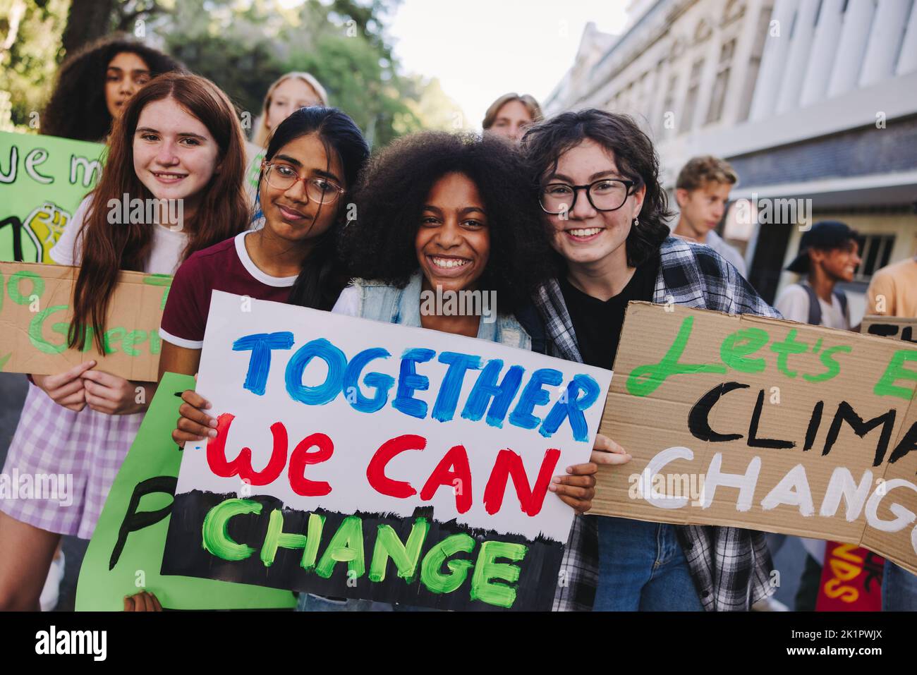 Chicas adolescentes felices sosteniendo un cartel durante una protesta por el cambio climático. Grupo de jóvenes activistas multiculturales marchando contra el calentamiento global. Diversos Foto de stock