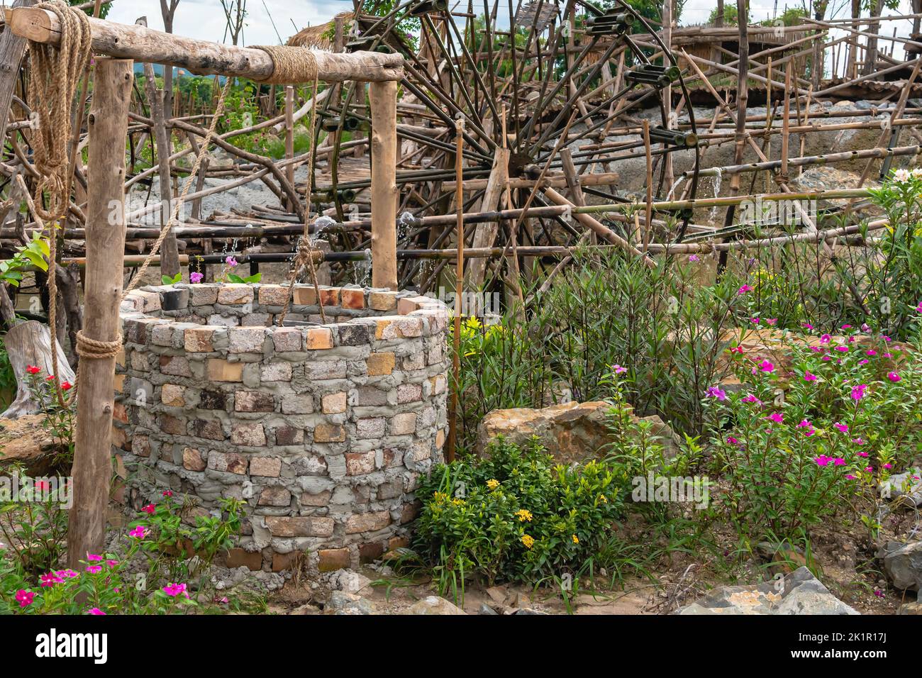 Hermoso pozo artesiano hecho de ladrillos con cemento y polea de rueda con  cubo de metal y cuerda en un ambiente tranquilo jardín. Retro piedra agua  pozo i Fotografía de stock -