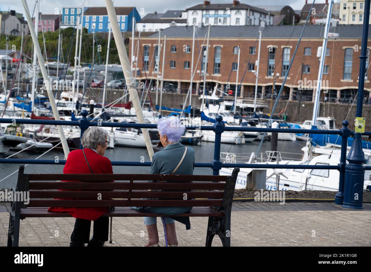 Gales, Pembrokeshire. Puerto deportivo de Milford Haven. Yachts y dos mujeres mayores se sentaron en un banco. Foto de stock