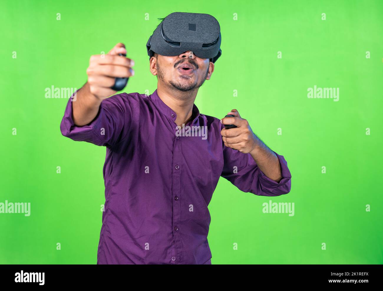 Joven emocionado con vr o auriculares de realidad virtual jugando videojuegos en metaverse utilizando joystick sobre fondo de pantalla verde - concepto de tecnología Foto de stock