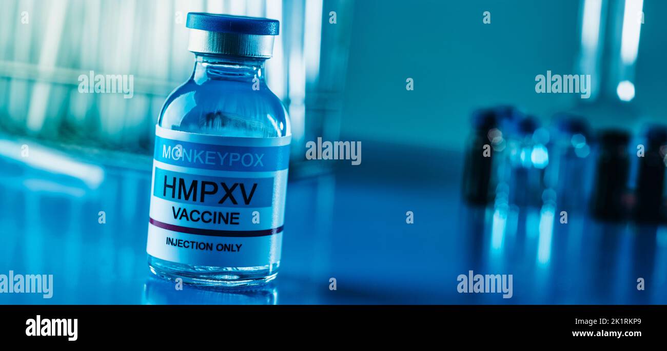 un vial de vacuna simulada contra la viruela del simio, en una mesa azul junto a algunas pruebas de tubo en un laboratorio, en un formato panorámico para utilizar como banner web o encabezado Foto de stock