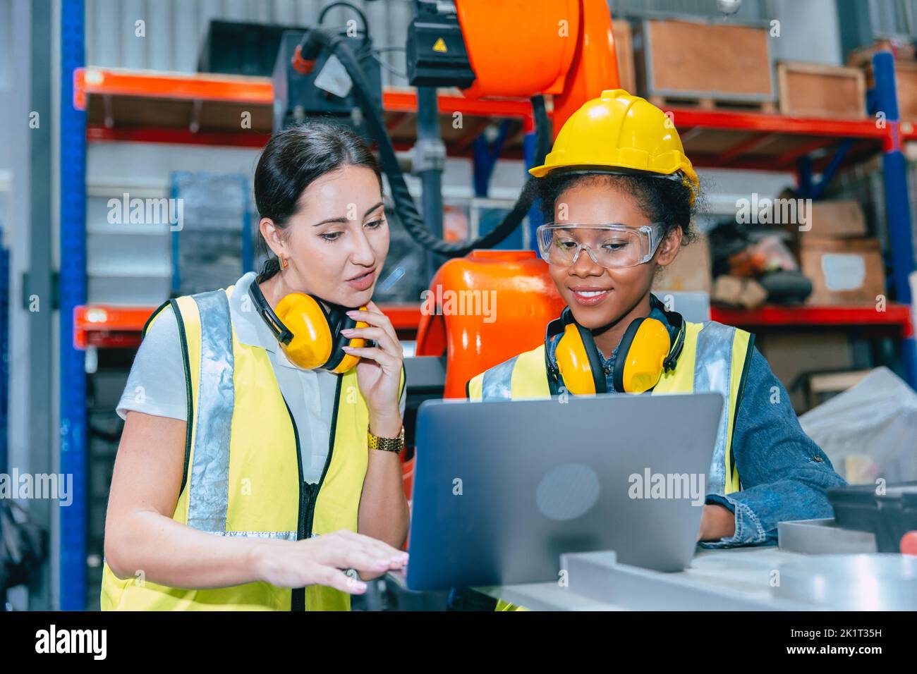 Formación conjunta del equipo de trabajo de las mujeres ingenieras en el trabajo en la moderna fábrica de máquinas de soldadura robótica avanzada. Foto de stock