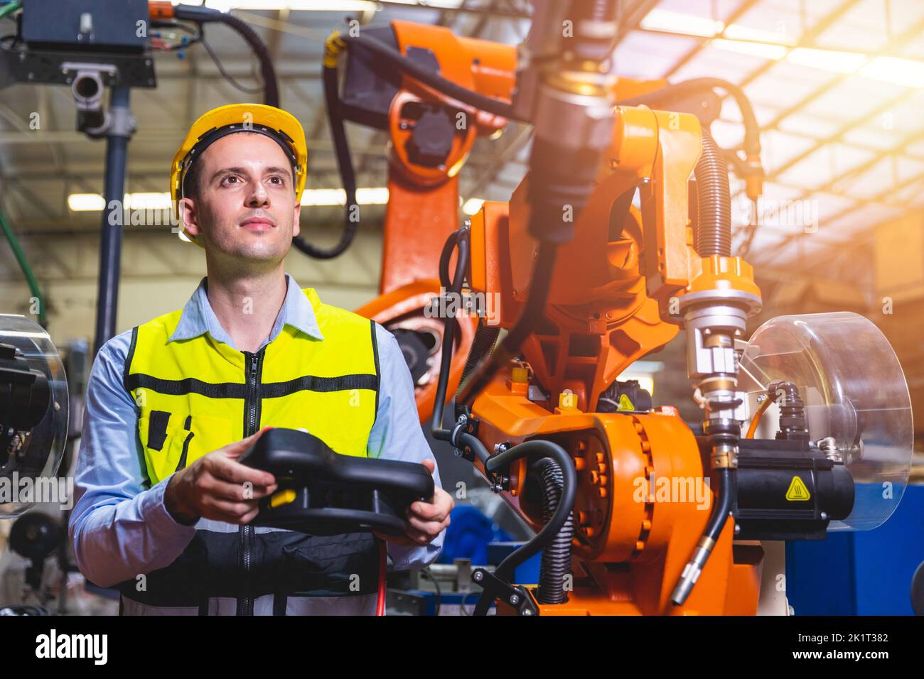 Ingeniero caucásico trabajador que trabaja en una fábrica de metal con un programador de máquina de soldadura por robot, controlador y monitor. Foto de stock