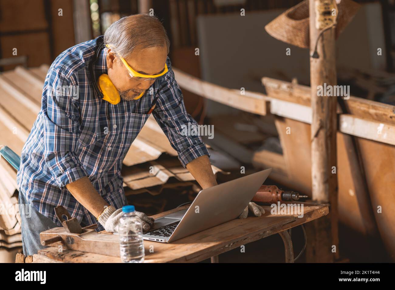 Trabajador mayor de madera constructor que utiliza un ordenador portátil para ayudar a diseñar trabajos de construcción. Foto de stock