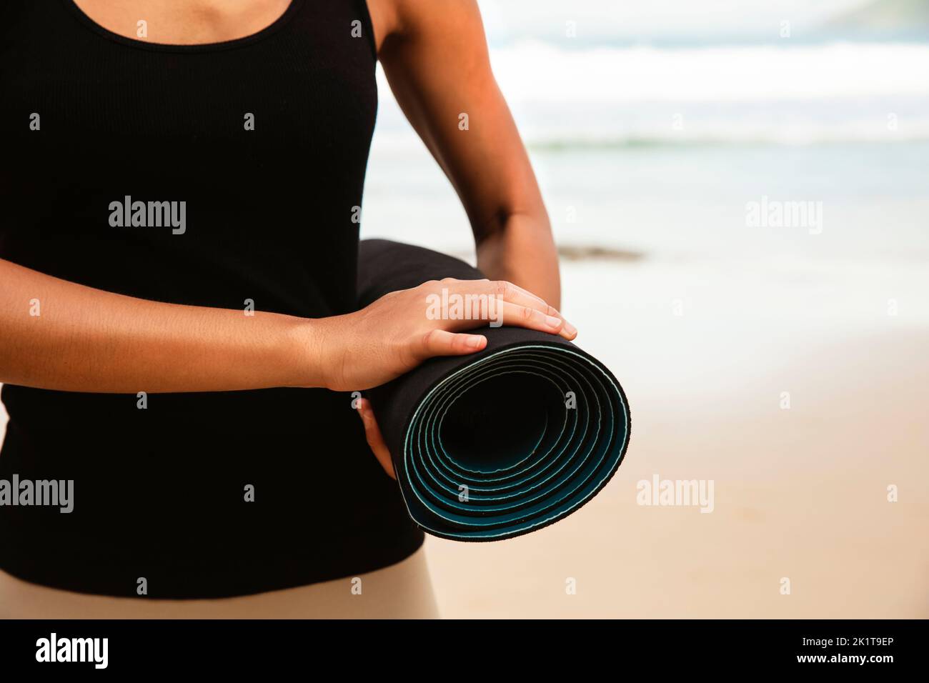 Mujer en la suite de deporte llevar colchón de yoga en la playa, Sport background.Healthy Lifestyle y viajes. Equipamiento deportivo femenino Foto de stock