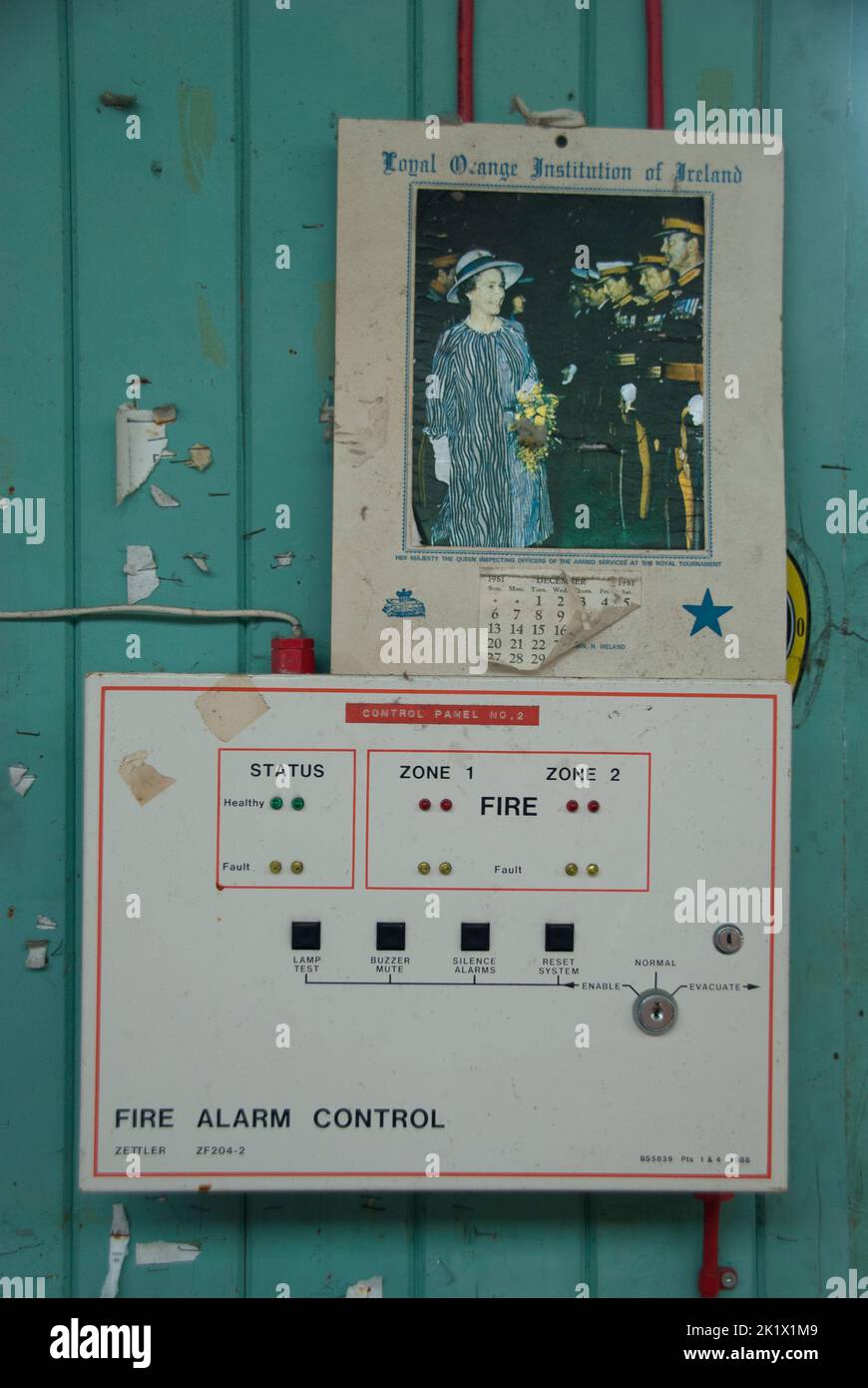 Panel de control de alarma de incendios con un calendario de la institución naranja leal de Irlanda que muestra la visita de la reina a Irlanda del Norte Foto de stock