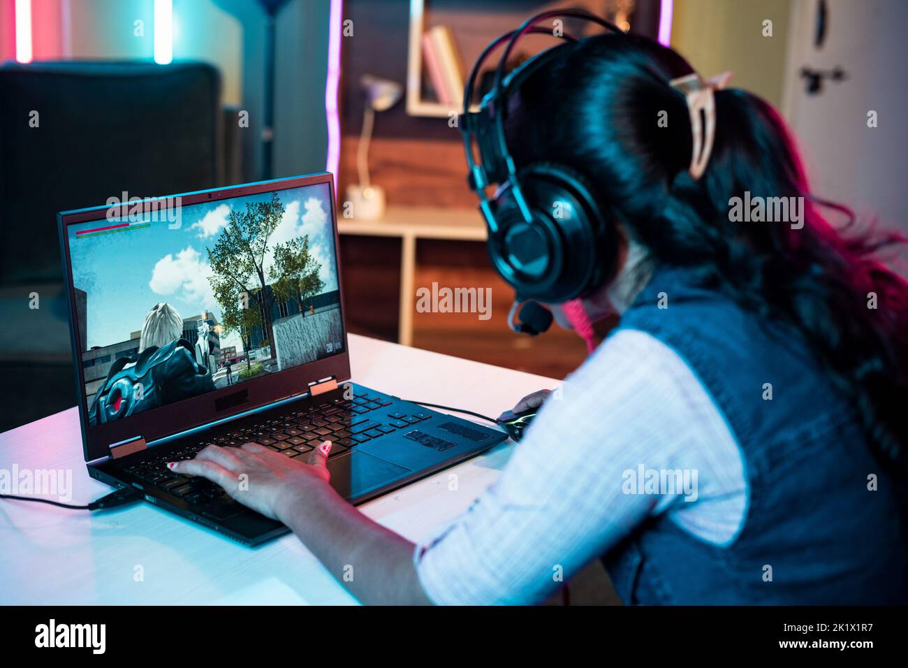 Hombro de mujer con auriculares jugando videojuegos en línea en el portátil en casa - concepto de transmisión en directo, la competencia y la tecnología. Foto de stock