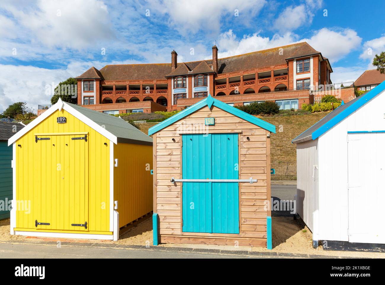 Coloridas cabañas en la playa frente al mar, edificio del hospital Barlet detrás, Felixstowe, Suffolk, Inglaterra, Reino Unido Foto de stock