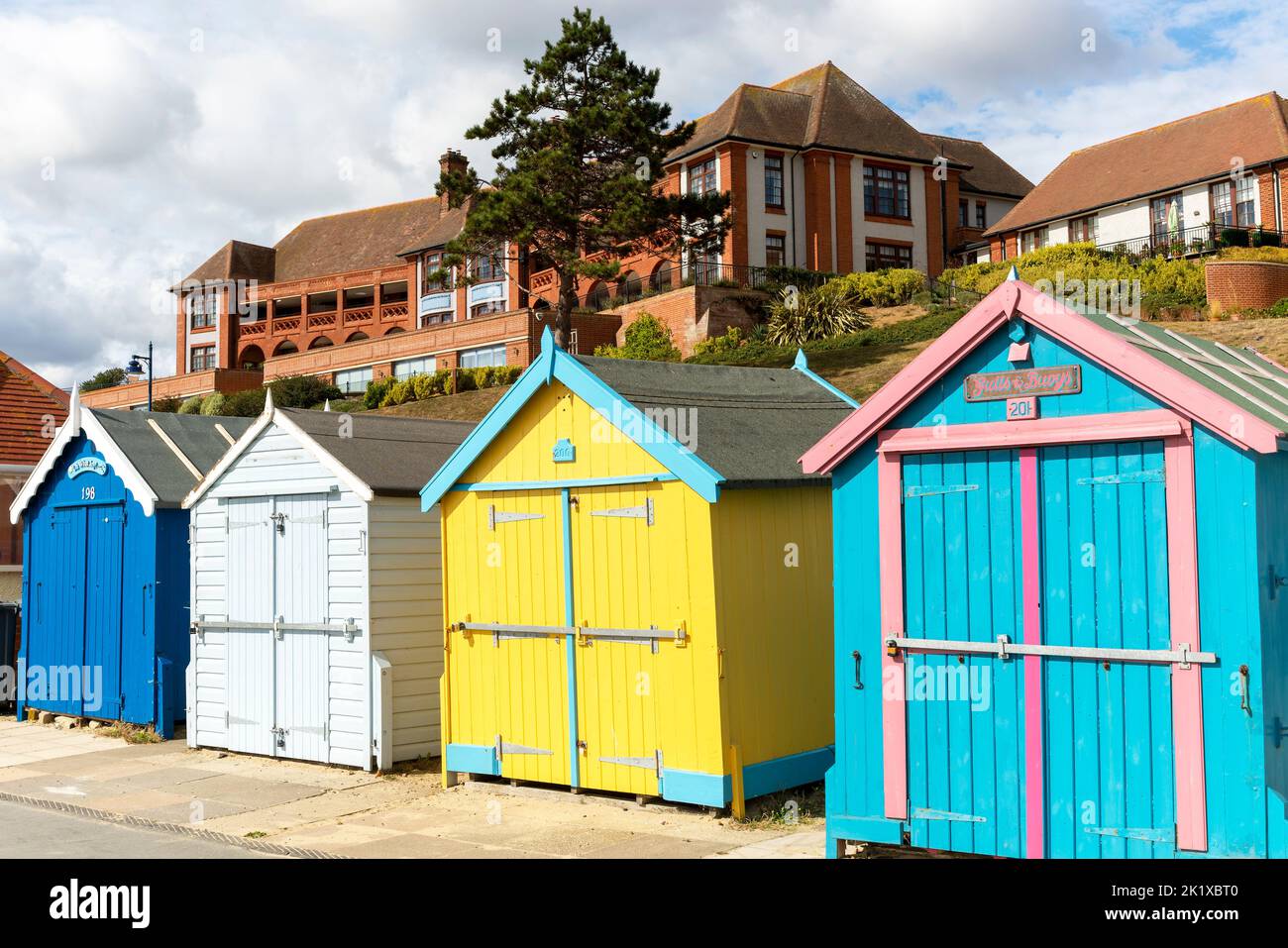 Coloridas cabañas en la playa frente al mar, edificio del hospital Barlet detrás, Felixstowe, Suffolk, Inglaterra, Reino Unido Foto de stock