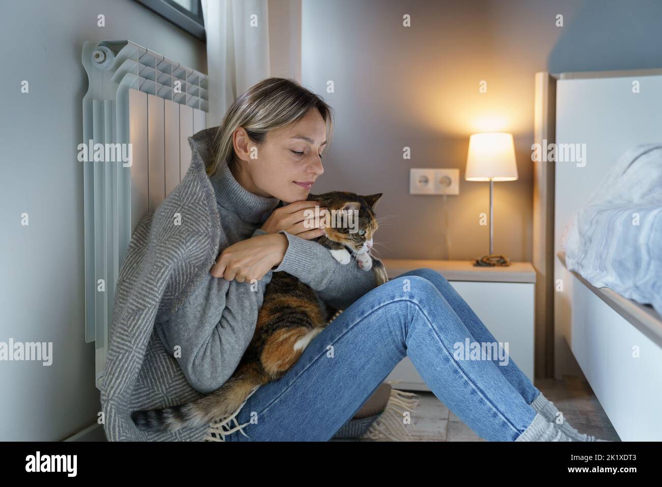 Mujer joven cubierta con manta caliente disfruta abrazando el gato y permaneciendo en casa con su mascota favorita Foto de stock