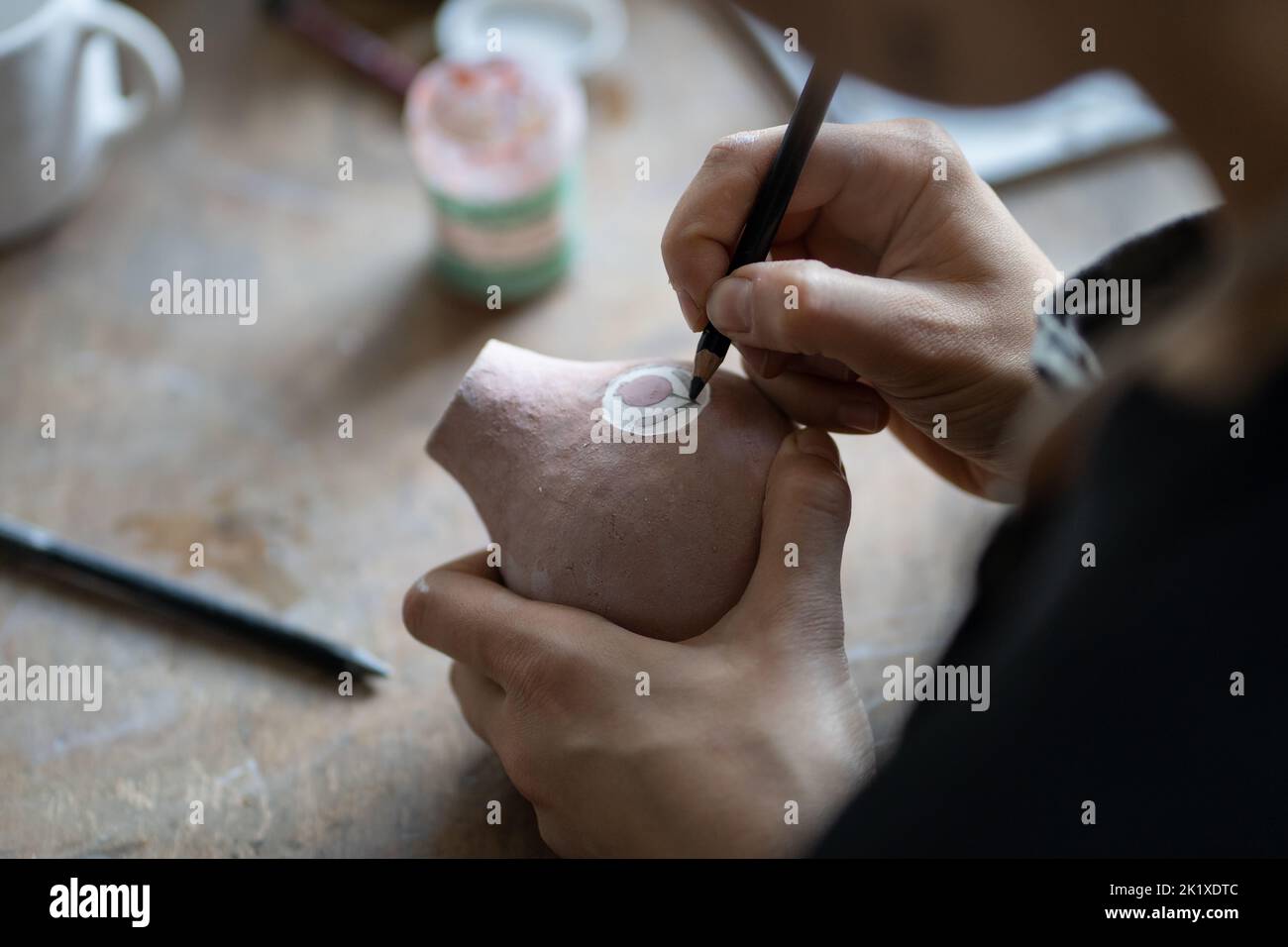 Craftsmaster hace interesante dibujo de boceto símbolo en la jarra usando lápiz para hacer el borrador Foto de stock