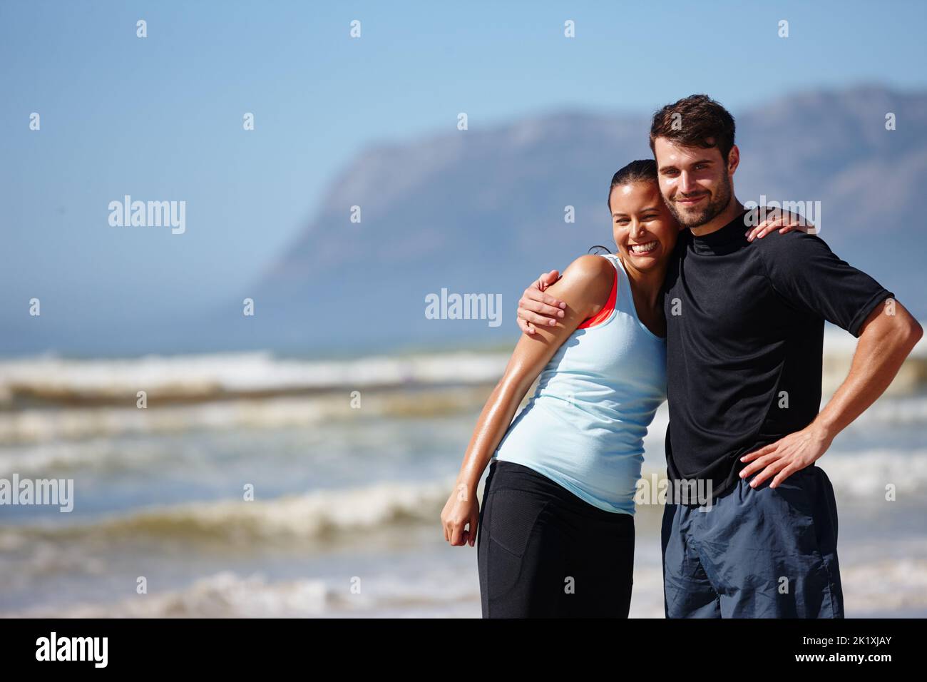 Nos encanta compartir nuestro entrenamiento de verano. Una pareja joven y cariñosa posando en equipo deportivo en la playa. Foto de stock