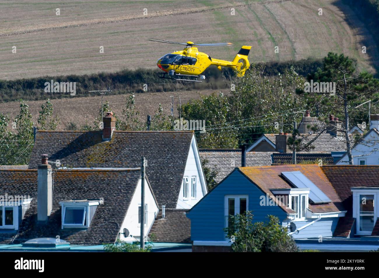 Burton Bradstock, Dorset, Reino Unido, 21st de septiembre de 2022. Un helicóptero de electricidad amarillo volando bajo sobre líneas eléctricas comprobando si hay fallos cerca de las casas de Burton Bradstock en Dorset. Crédito de la imagen: Graham Hunt/Alamy Live News Foto de stock