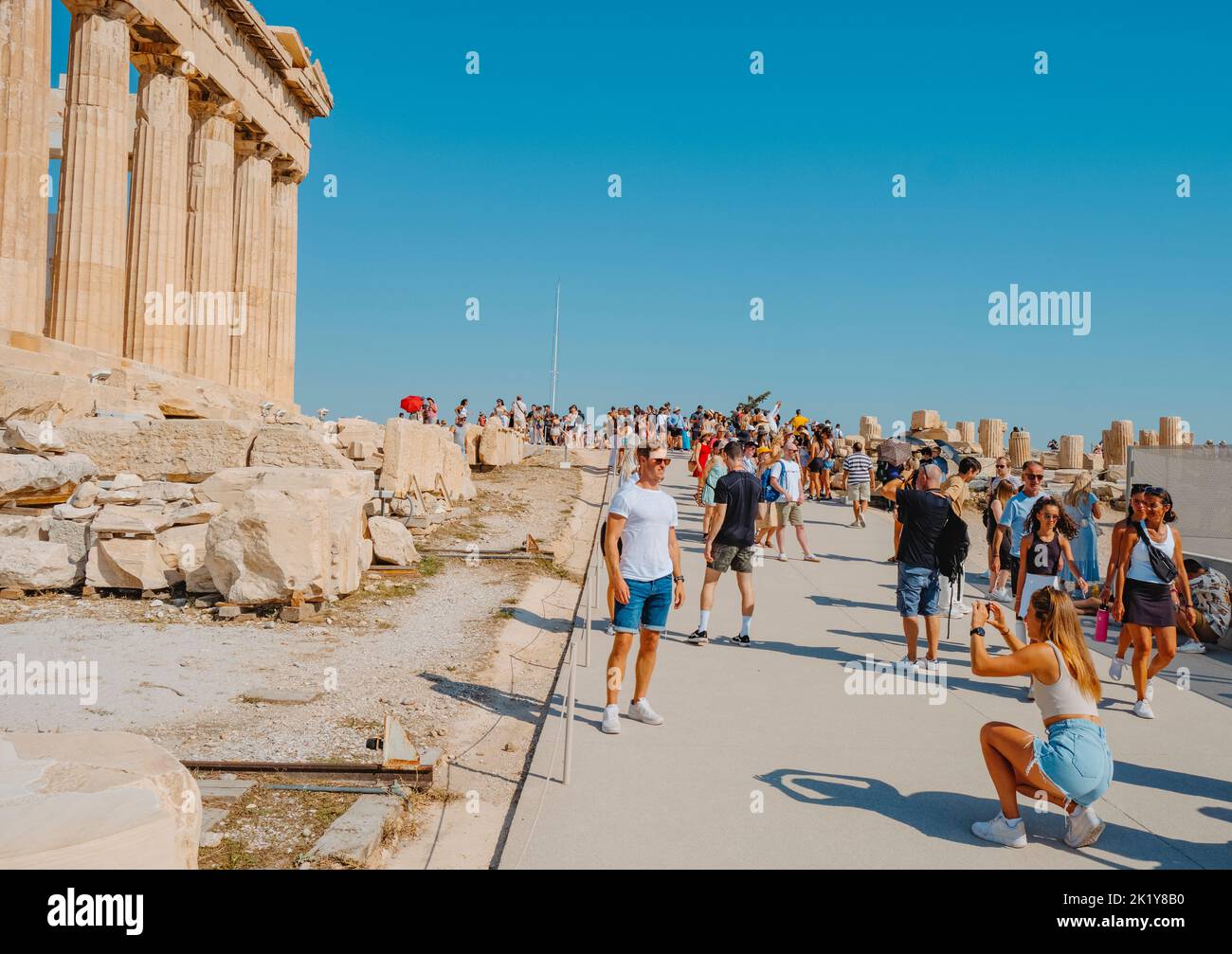 Atenas, Grecia - 30 de agosto de 2022: Una joven toma una foto de un joven delante de los restos del famoso Partenón, en la Acrópolis de Atenas Foto de stock