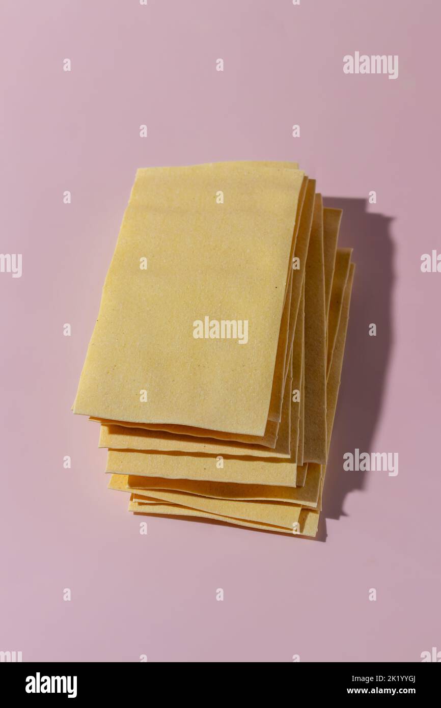 Láminas de pasta lasaña seca sin cocinar sobre fondo rosa Foto de stock