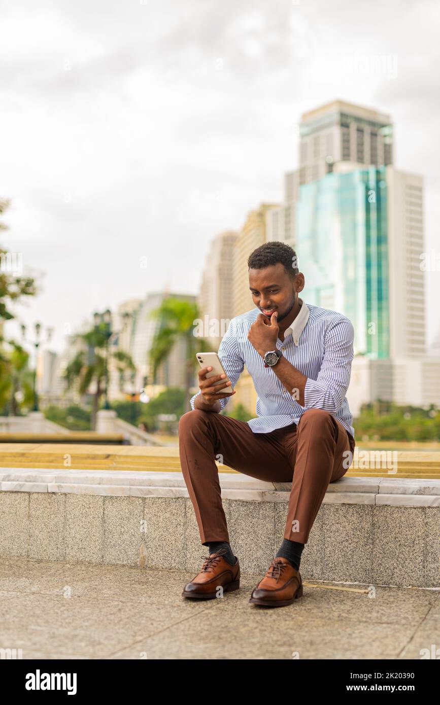 Hermoso hombre de negocios negro en el parque utilizando el teléfono móvil Foto de stock