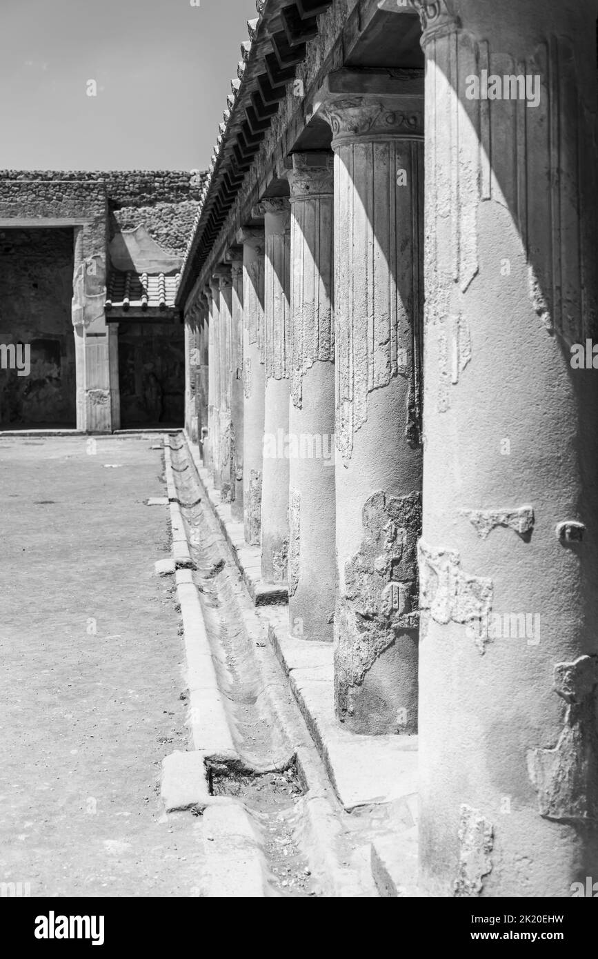 Foto en blanco y negro que muestra en perspectiva la columnata exterior del antiguo templo romano en Pompeya Foto de stock