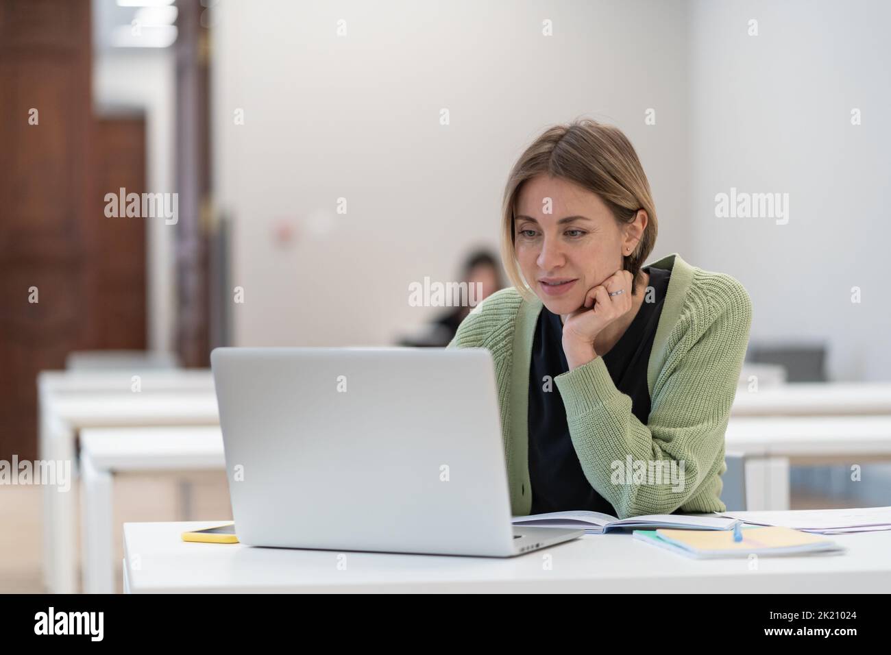 Mujer de mediana edad que utiliza un portátil para el aprendizaje electrónico, estudiante madura viendo seminario web en la biblioteca Foto de stock