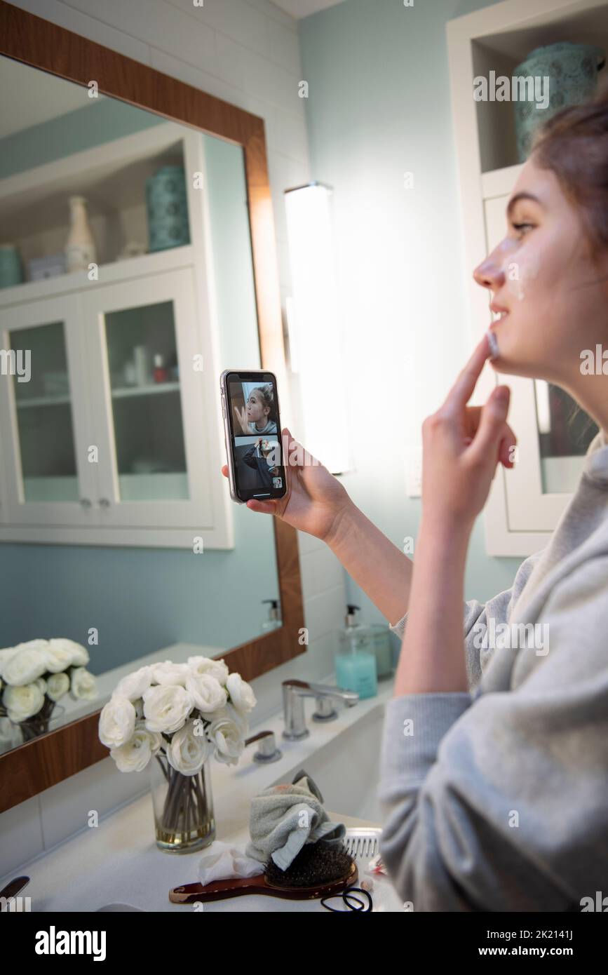 Chica adolescente aplicando máscara facial con amigos por chat de vídeo Foto de stock