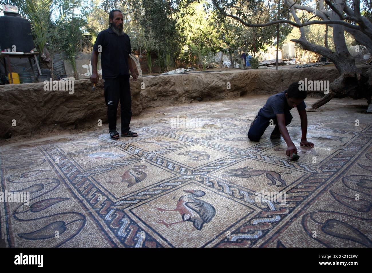 Campamento Al Bureij, Gaza. 21st de Sep de 2022. El agricultor palestino Salman al-Nabahin, de 52 años, y su hijo Ahmad, de 16 años, limpian un suelo de mosaico que descubrió en su granja y que data de la época bizantina, según los funcionarios, en el campamento Al-Bureij, en la zona central de la Franja de Gaza, el miércoles 21 de septiembre de 2022. El Ministerio de Turismo y Antigüedades de Palestina anunció el descubrimiento del mosaico, que será protegido y un proyecto de excavación comenzará Lo antes posible.. Foto de Ismael Mohamad/UPI Crédito: UPI/Alamy Live News Foto de stock