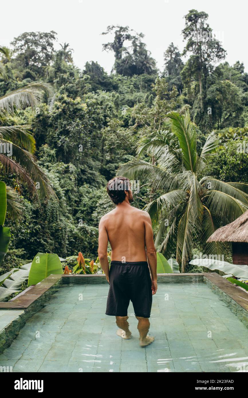 Imagen trasera de un hombre joven parado en la piscina y mirando una vista. Modelo masculino en el complejo turístico. Foto de stock