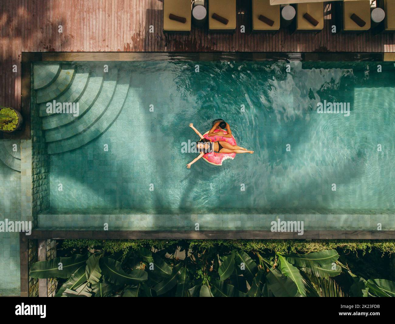 Vista aérea de una pareja disfrutando de la piscina del complejo. Mujer joven tumbada en un anillo inflable con un hombre en la piscina del complejo. Foto de stock