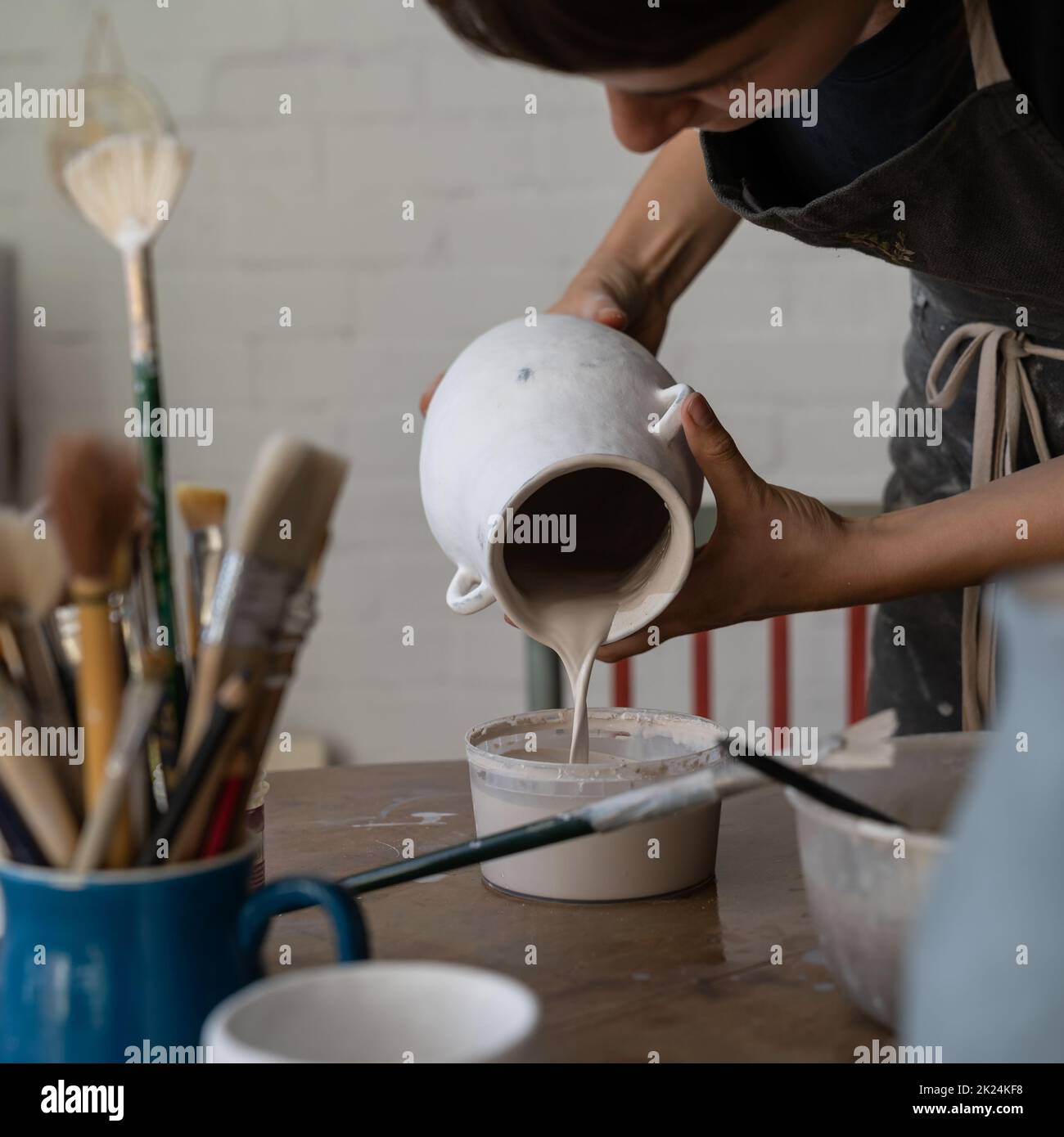 La artesana limpia el recipiente blanco dentro lavando lejos y vertiendo las sobras en el tazón de plástico en el estudio Foto de stock
