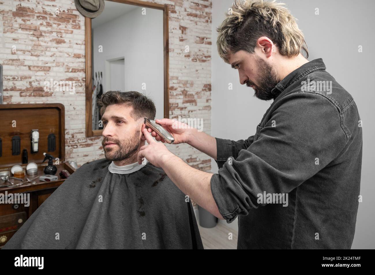 Hombre barbero cortando pelo de cliente masculino con cortapelos