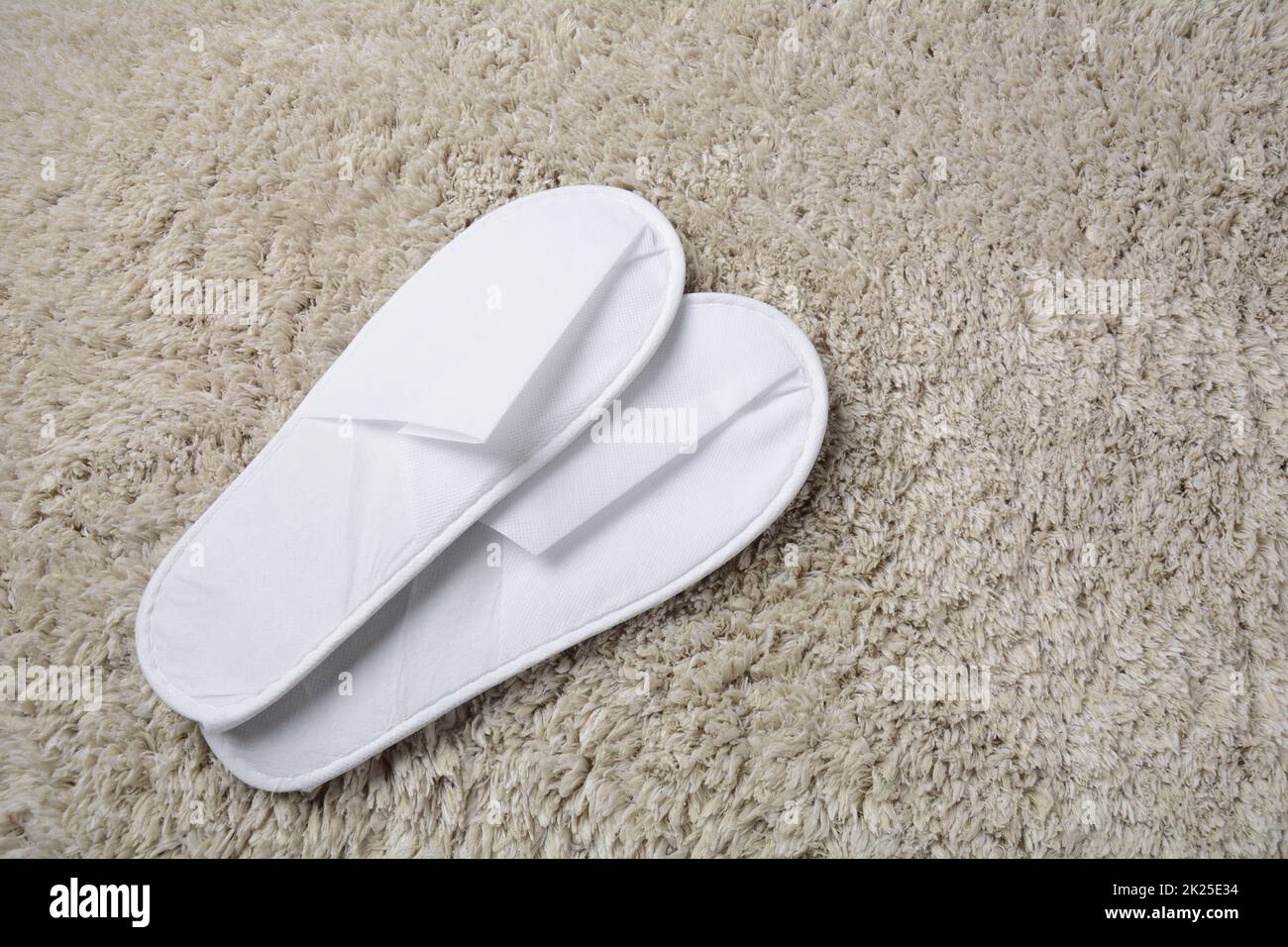 Zapatillas blancas sobre alfombrilla gris. Hay un par de zapatillas cómodas en la habitación del hotel Foto de stock