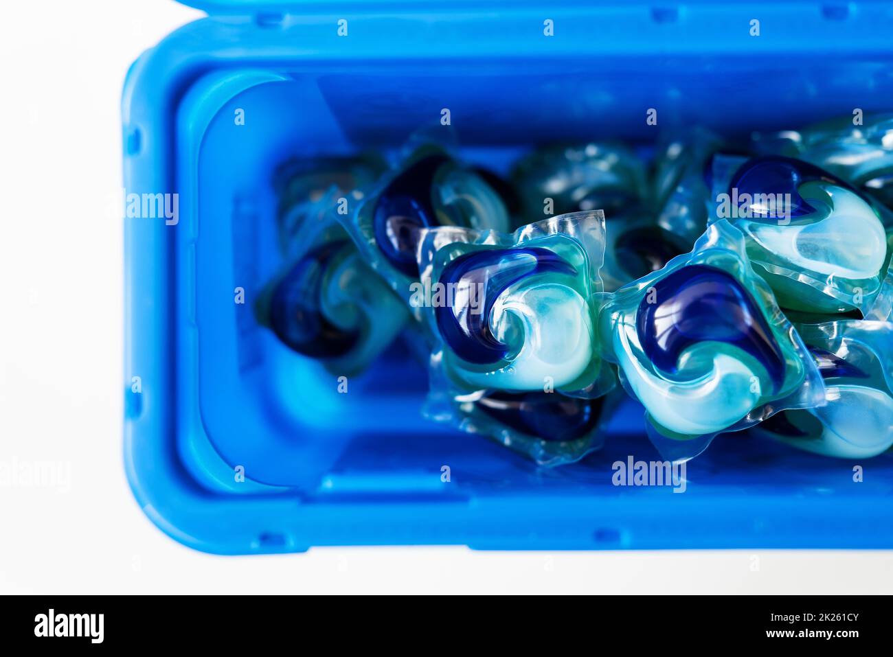 Los polvos de lavado en cápsulas de varios colores se encuentran en una caja de plástico azul. El concepto de lavado y limpieza. Foto de stock