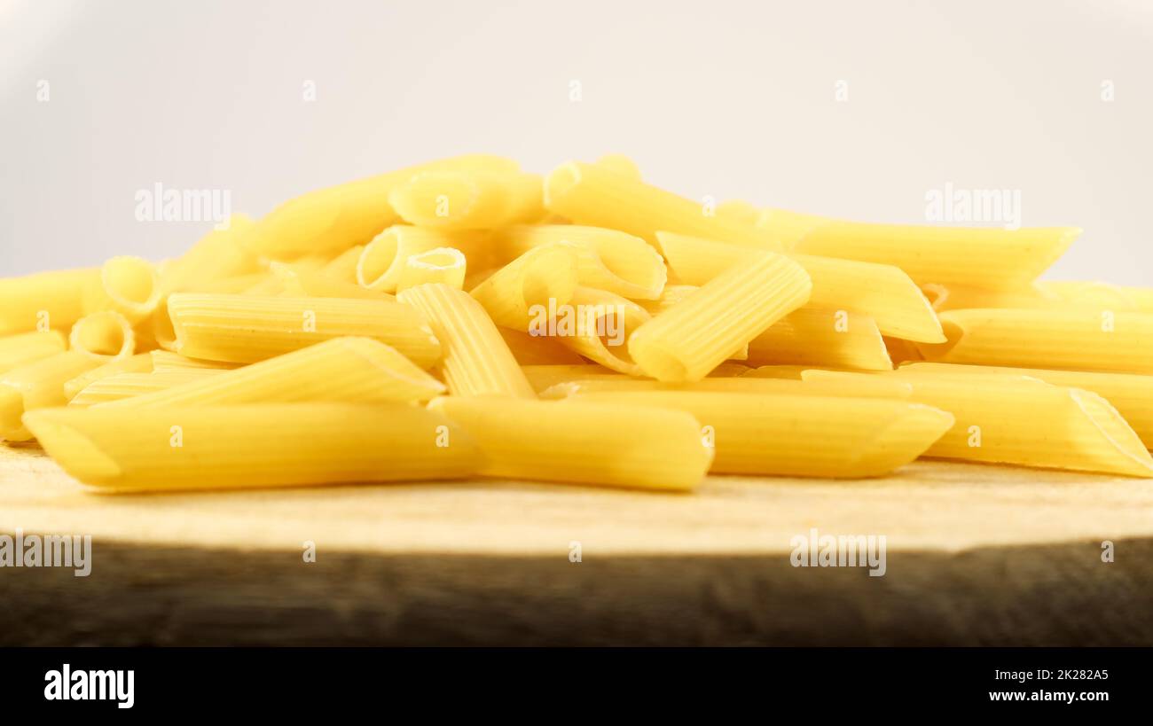 La pasta cruda Penne Rigate es una pasta corta con cortes oblicuos y una superficie estriada. Pasta tradicional italiana. Pasta de fondo. Vista lateral de un ingrediente italiano en un plato de madera. Foto de stock