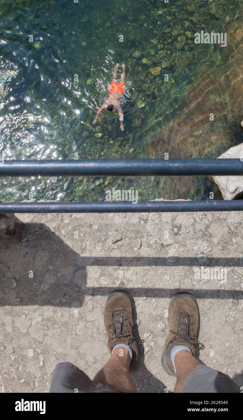 Trekker observando a nadador desde el parapeto del puente. Piscina natural de La Maquina, aguas cristalinas en el corazón de la comarca de La Vera, Cáceres, Extremadura Foto de stock