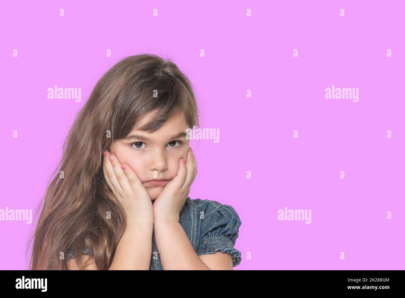 Bronceada triste niña está posando sobre fondo rosa. Foto de stock