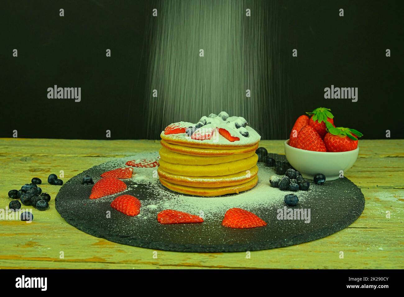 Panqueques con frutas bayas sobre fondo negro. Tortitas frescas. Arándanos, fresas en panqueques. Espolvoree azúcar glaseado en los panqueques. Pizarra y fondo de madera Foto de stock