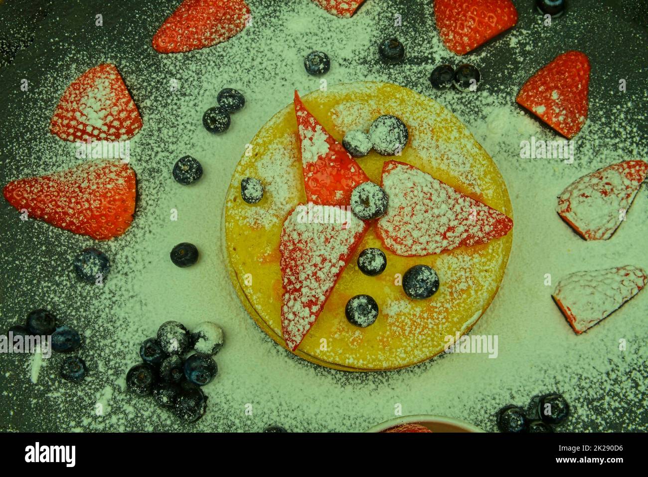 Tortitas con frutas bayas sobre fondo negro. Tortitas frescas. Arándanos, fresas y azúcar glaseado en tortitas. Capa plana Foto de stock