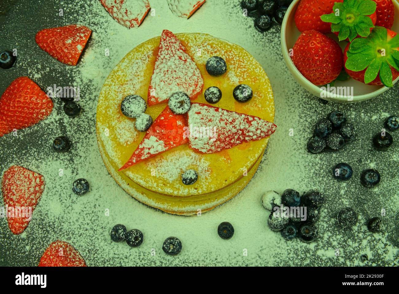 Saludable desayuno de verano, tortitas americanas clásicas caseras con bayas frescas y azúcar glasé. Arándanos y fresas en panqueques. Fondo negro, plano Foto de stock