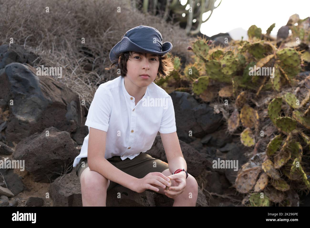 Retrato de un adolescente en una camisa de polo y un sombrero contra el fondo de cactus. Foto de stock