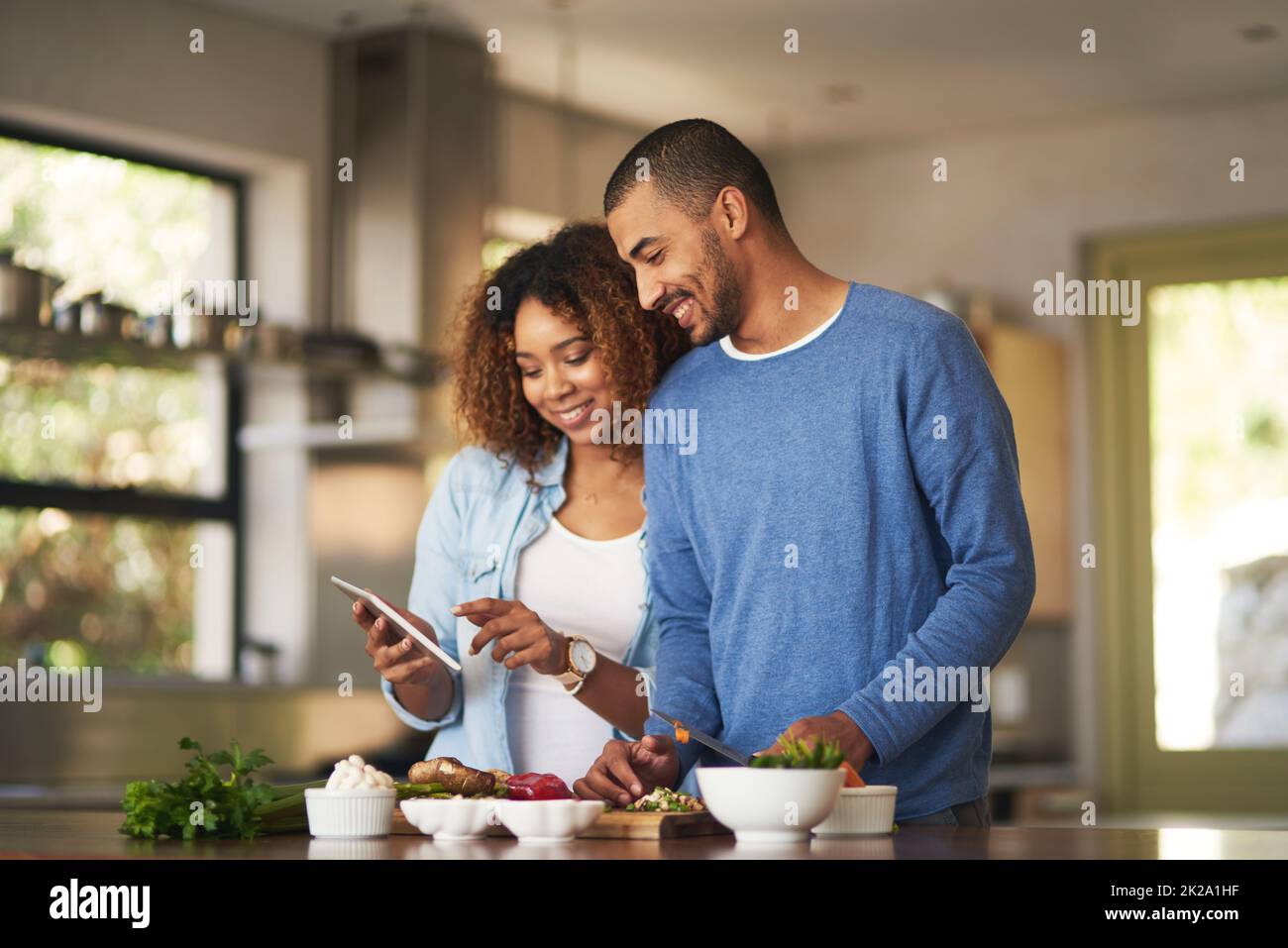 Usando una receta en línea paso a paso. Foto de una joven pareja feliz usando una tableta digital mientras preparaba una comida saludable juntos en casa. Foto de stock