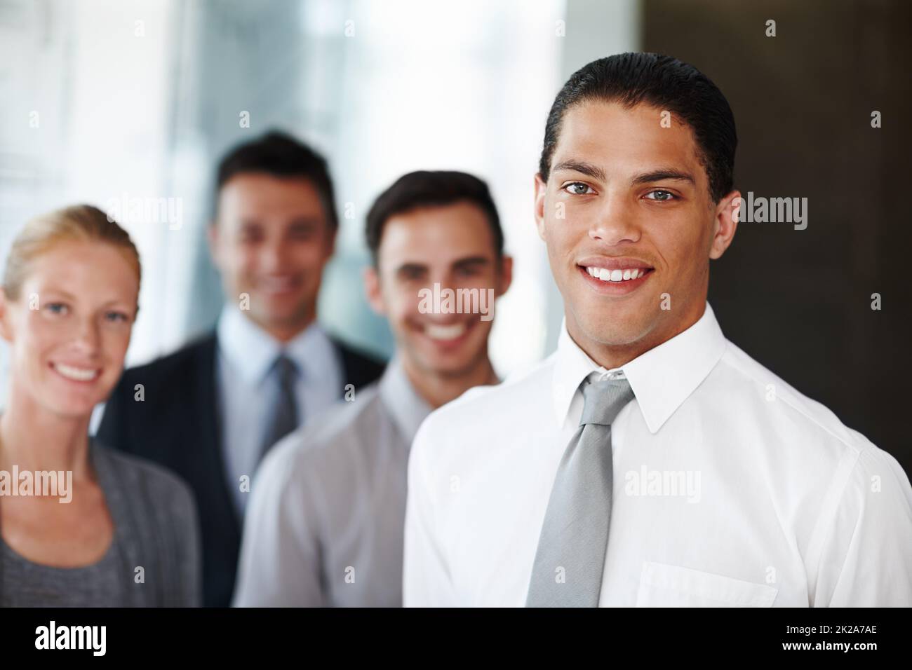 Positivo sobre el negocio corporativo. Un hombre de negocios afroamericano mirando la cámara con sus compañeros de trabajo en el fondo. Foto de stock