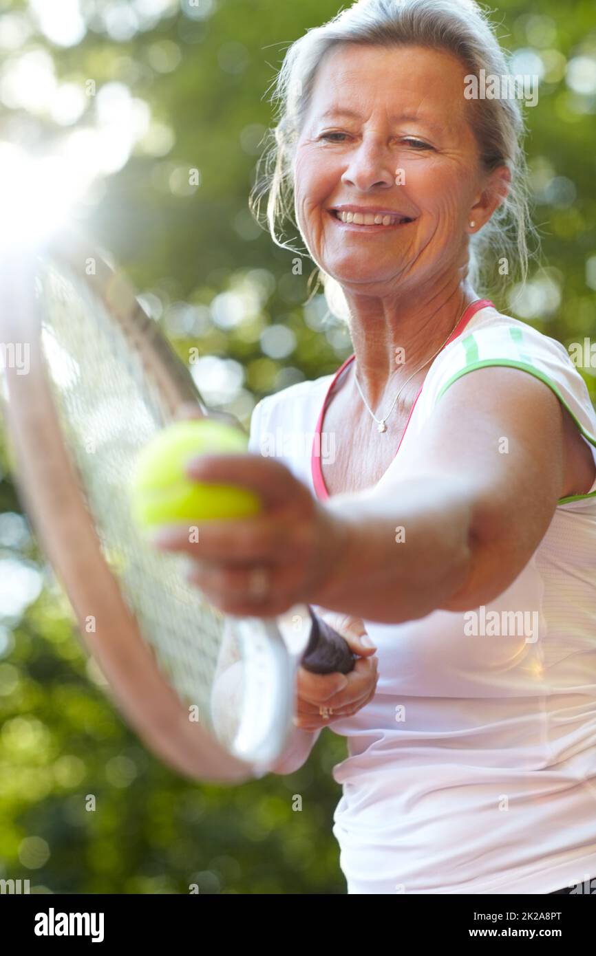 He tenido años de práctica para perfeccionar mi servicio. Sonriente mujer mayor preparándose para servir - Tenis. Foto de stock