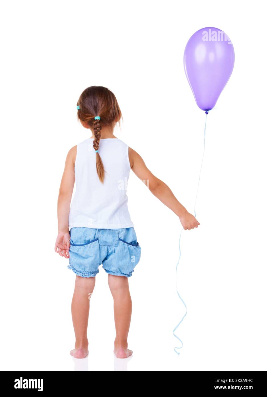 Dejando una fiesta de cumpleaños. Vista trasera completa de una niña sosteniendo un globo. Foto de stock