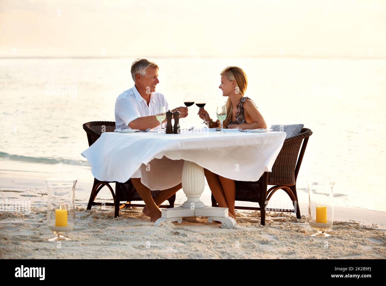 Pareja romántica celebrando con vino en la playa. Foto de una pareja adulta disfrutando de una cena romántica en la playa. Foto de stock