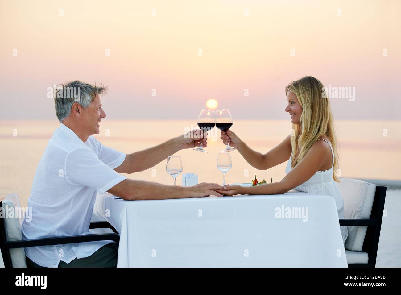 Heres para nosotros. Foto de una pareja adulta disfrutando de una cena romántica en la playa. Foto de stock