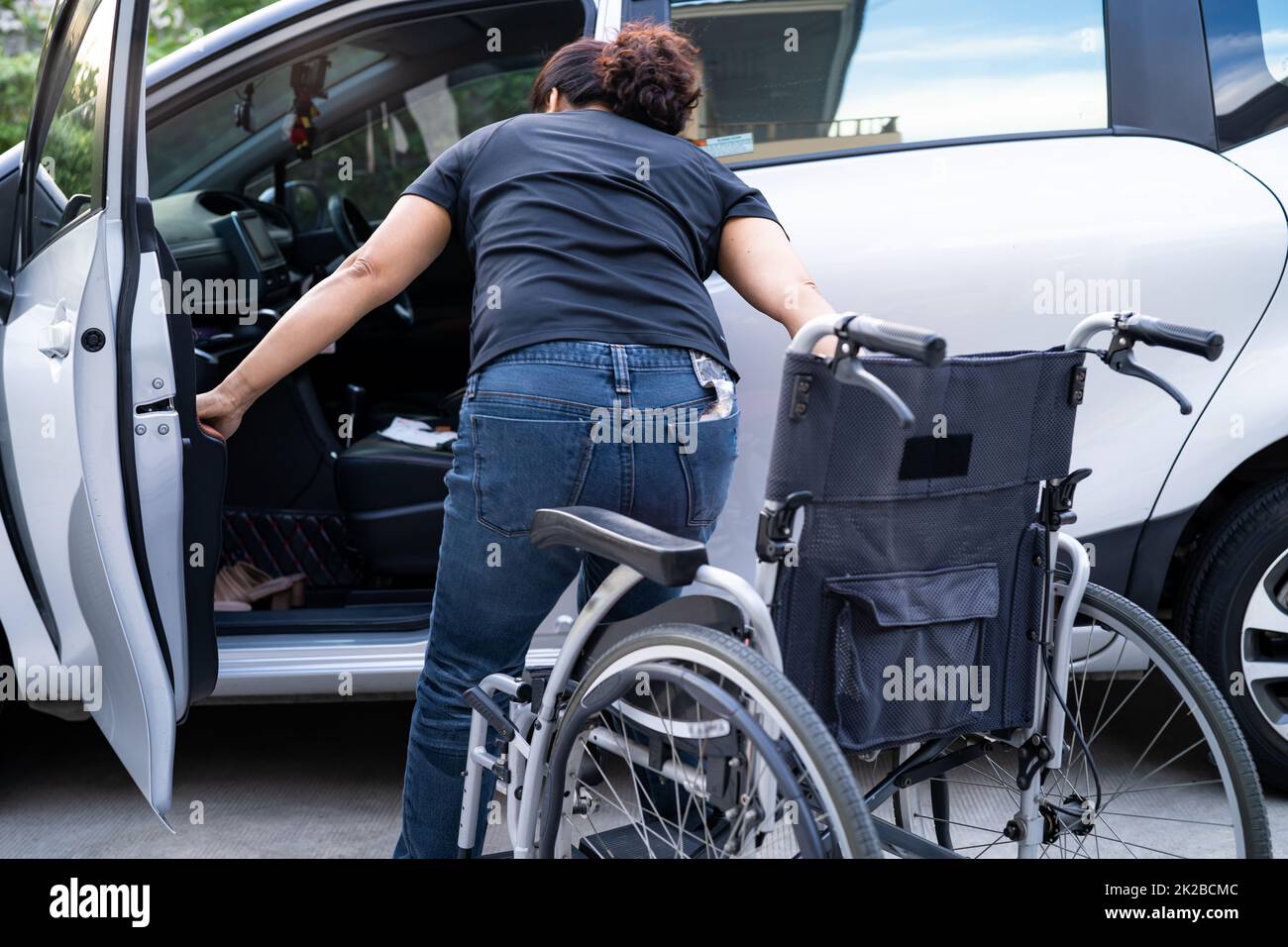 Mujer asiática que dobla y levanta la silla de ruedas en su coche. Concepto de accesibilidad. Foto de stock